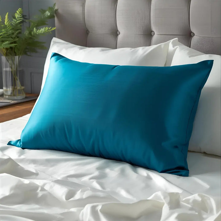 une taie d'oreiller en soie bleu paon sur lit blanc 