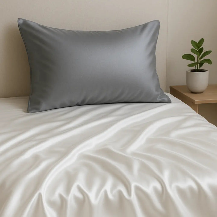 Taie d’oreiller en soie gris foncé 19 Momme sur lit avec draps blancs, tête de lit beige et table de chevet en bois avec plante verte.